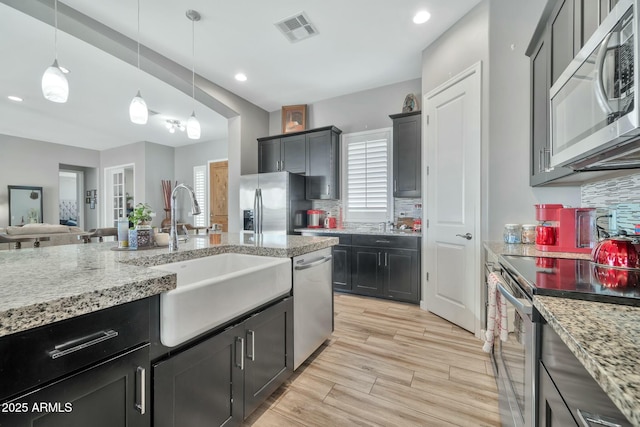 kitchen with backsplash, sink, light stone countertops, decorative light fixtures, and stainless steel appliances