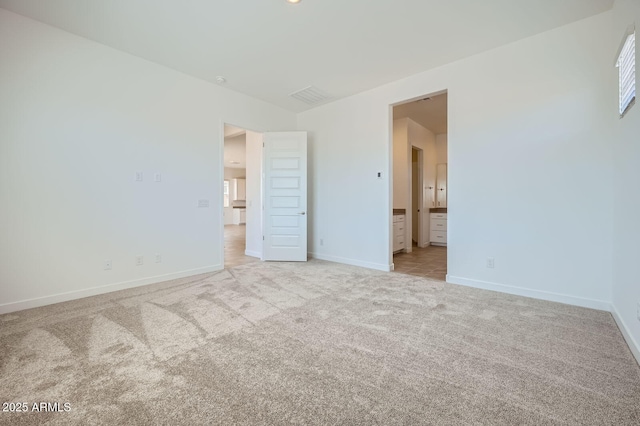 unfurnished bedroom featuring light colored carpet, baseboards, and ensuite bathroom