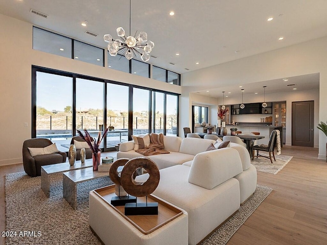 living room featuring light wood-type flooring, an inviting chandelier, and a high ceiling