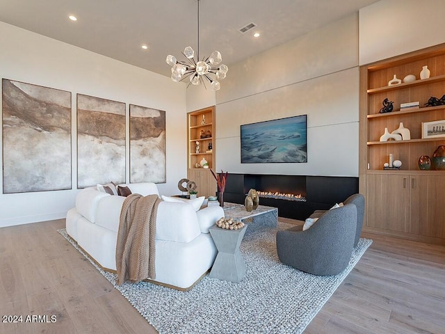 living room featuring light wood-type flooring, a chandelier, and built in shelves