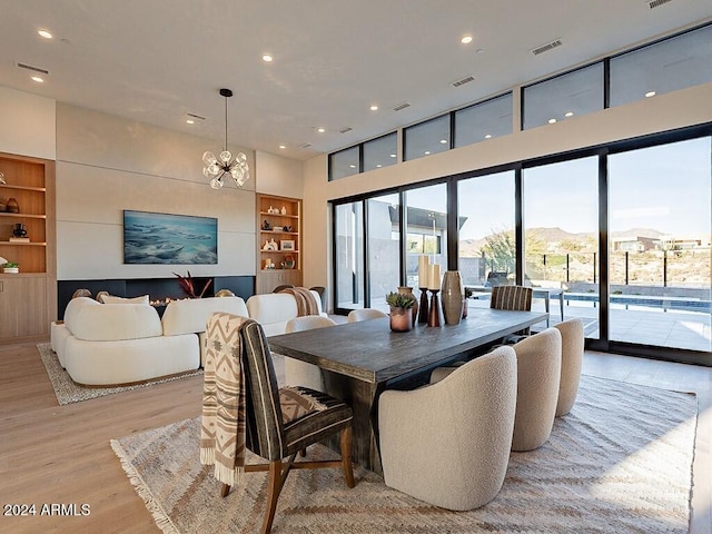 dining space with a notable chandelier, a mountain view, a towering ceiling, light wood-type flooring, and built in features