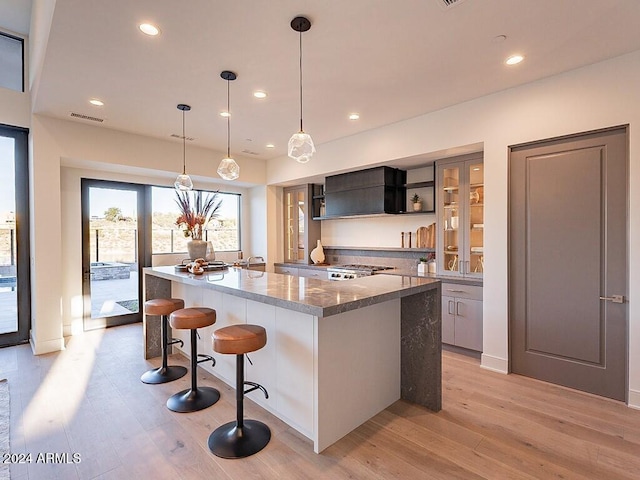 kitchen with light hardwood / wood-style flooring, an island with sink, pendant lighting, a kitchen bar, and dark stone countertops