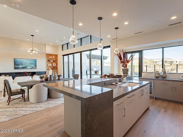 kitchen with a center island with sink, sink, light hardwood / wood-style floors, white cabinets, and hanging light fixtures