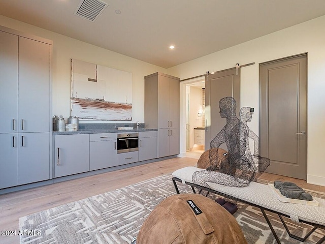 kitchen with stainless steel oven, light hardwood / wood-style floors, and a barn door