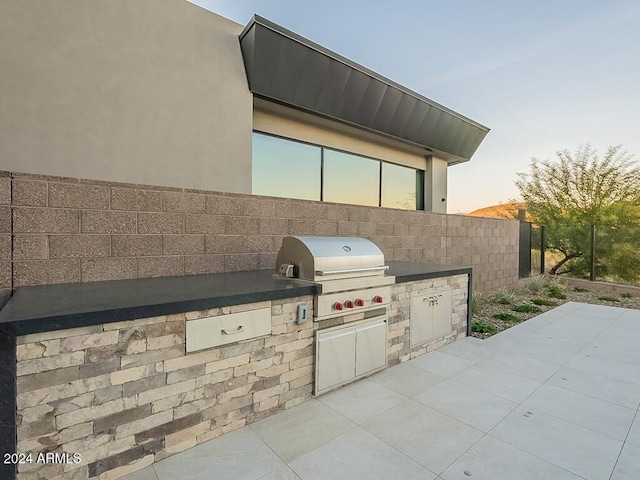 patio terrace at dusk featuring a grill and exterior kitchen