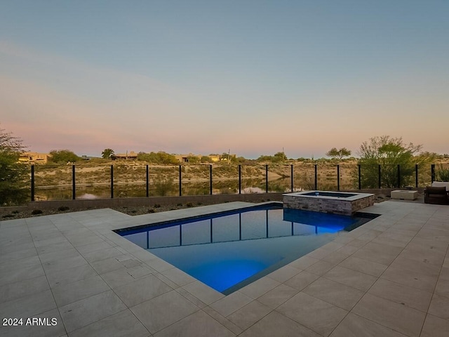 pool at dusk featuring a patio area and an in ground hot tub