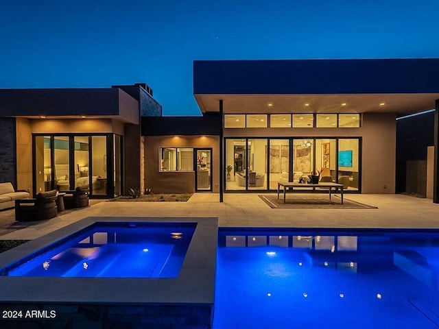 pool at twilight with a patio area, an in ground hot tub, and an outdoor hangout area