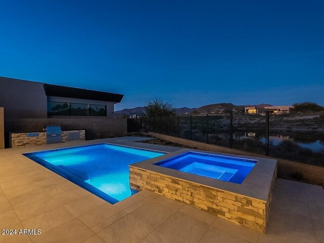 view of pool with an in ground hot tub, a water and mountain view, an outdoor kitchen, a patio area, and a grill