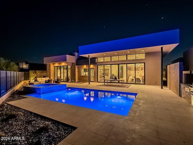 pool at night with an in ground hot tub and a patio