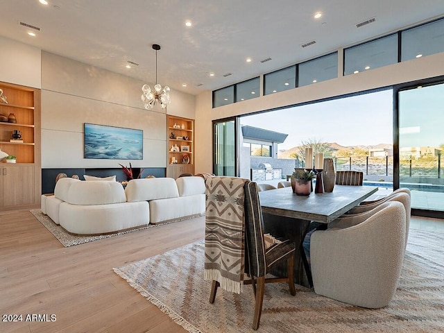 dining room with an inviting chandelier, light hardwood / wood-style flooring, built in shelves, expansive windows, and a high ceiling