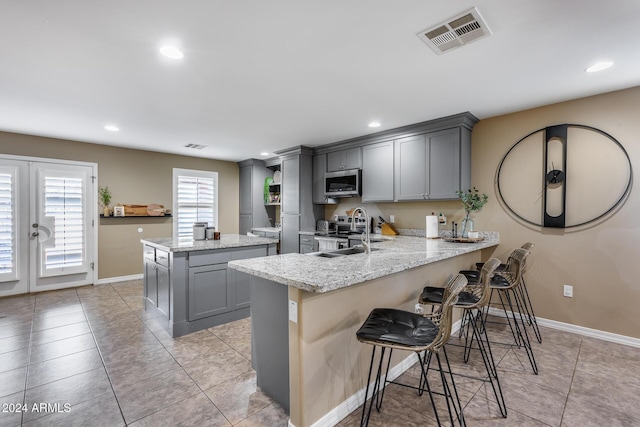 kitchen featuring gray cabinetry, sink, light stone counters, kitchen peninsula, and appliances with stainless steel finishes