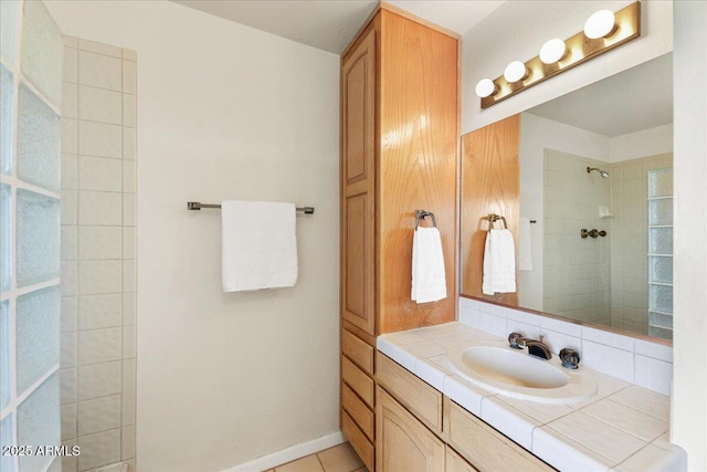 full bath featuring vanity, baseboards, tile patterned flooring, and tiled shower