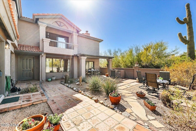 rear view of house with a tile roof, stucco siding, a chimney, a balcony, and a patio