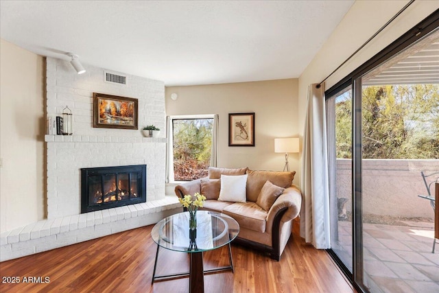 living area featuring a brick fireplace, plenty of natural light, and wood finished floors