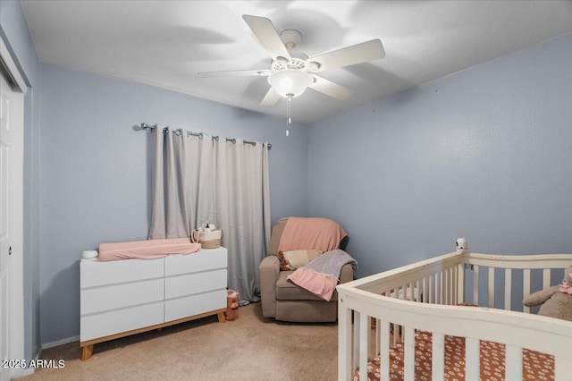 carpeted bedroom featuring a nursery area and ceiling fan