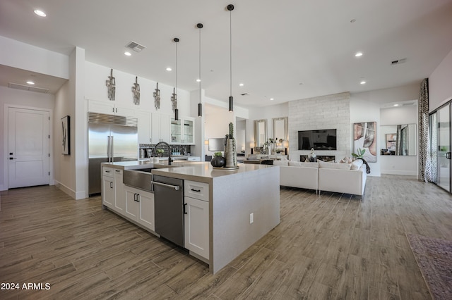 kitchen with an island with sink, open floor plan, stainless steel appliances, white cabinetry, and a sink