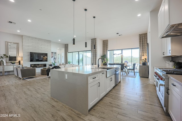 kitchen featuring an island with sink, appliances with stainless steel finishes, hanging light fixtures, white cabinetry, and a sink