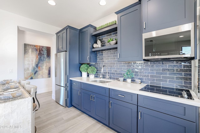 kitchen with stainless steel appliances, a sink, light wood-style floors, backsplash, and open shelves