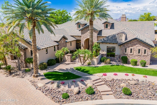 view of front of home with a front yard, stone siding, stucco siding, a chimney, and a tile roof