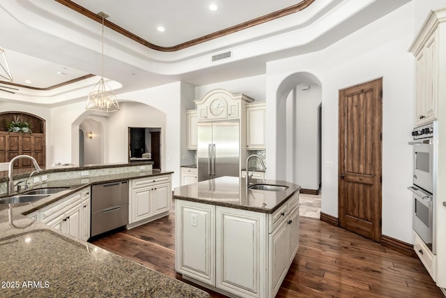 kitchen featuring arched walkways, a tray ceiling, appliances with stainless steel finishes, and a sink