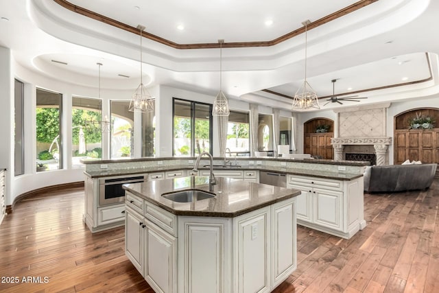 kitchen with a large fireplace, a center island with sink, a sink, an inviting chandelier, and a tray ceiling