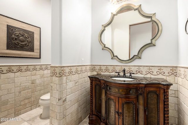bathroom featuring vanity, a wainscoted wall, toilet, and tile walls
