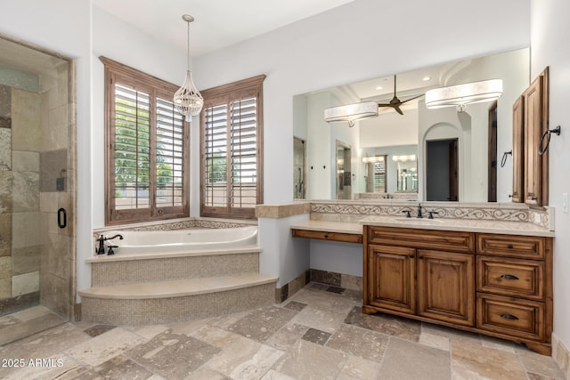 full bathroom featuring vanity, ceiling fan with notable chandelier, a shower stall, a bath, and stone tile flooring