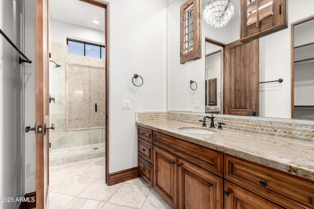 bathroom with tile patterned flooring, vanity, baseboards, a shower stall, and a notable chandelier