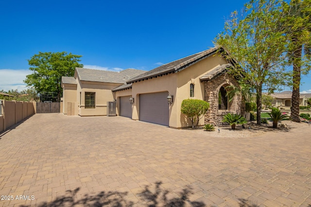 mediterranean / spanish-style house featuring an attached garage, stucco siding, stone siding, and fence