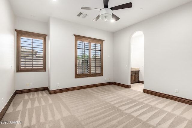 spare room with ceiling fan, light colored carpet, arched walkways, baseboards, and visible vents