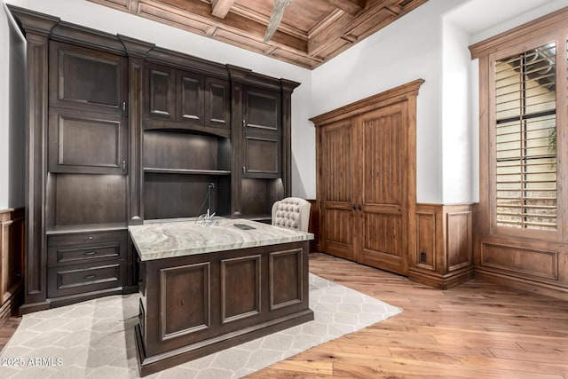 office space featuring light wood-type flooring, coffered ceiling, a wainscoted wall, and beam ceiling