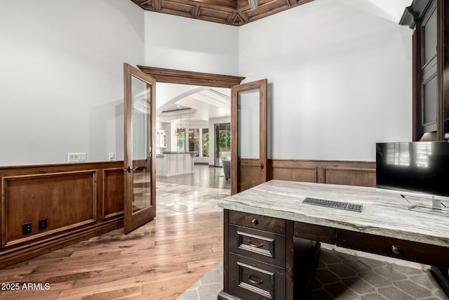home office featuring french doors, arched walkways, wainscoting, and light wood finished floors
