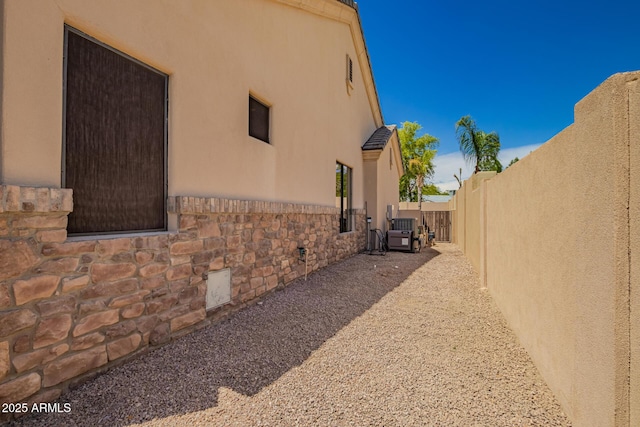view of side of property featuring stucco siding, stone siding, and fence