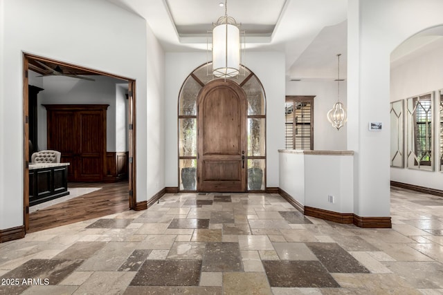 entrance foyer featuring arched walkways, baseboards, an inviting chandelier, a tray ceiling, and stone tile floors