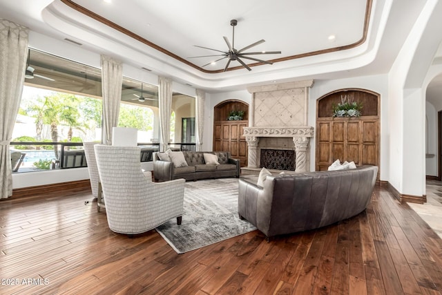 living room featuring a raised ceiling, arched walkways, a ceiling fan, baseboards, and hardwood / wood-style flooring