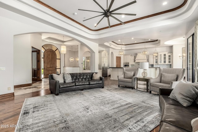 living area featuring a raised ceiling, ornamental molding, ceiling fan with notable chandelier, and arched walkways