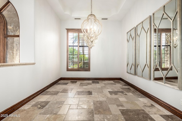unfurnished dining area with baseboards, an inviting chandelier, a raised ceiling, and stone tile flooring