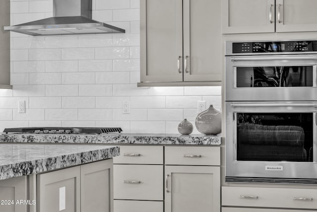 kitchen featuring stainless steel appliances, wall chimney exhaust hood, decorative backsplash, and light stone countertops