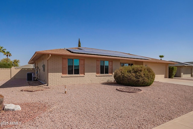 view of front facade featuring central AC unit, an attached garage, brick siding, driveway, and roof mounted solar panels