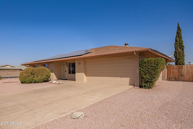 ranch-style house featuring brick siding, concrete driveway, an attached garage, roof mounted solar panels, and fence