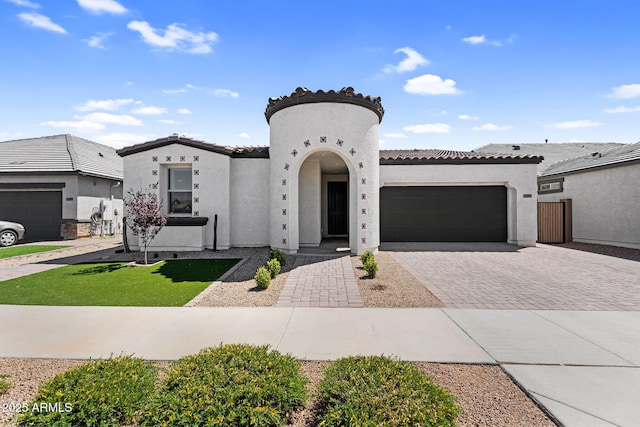 mediterranean / spanish house with a tile roof, decorative driveway, a garage, a front yard, and stucco siding