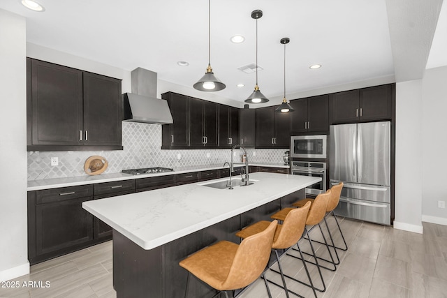 kitchen with wall chimney range hood, a sink, a breakfast bar area, stainless steel appliances, and visible vents