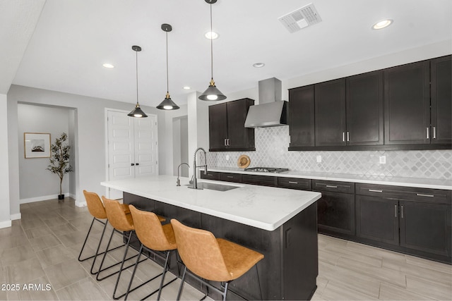 kitchen with backsplash, wall chimney range hood, visible vents, a sink, and stainless steel gas cooktop