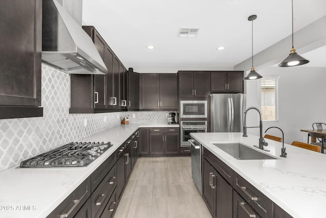 kitchen featuring wall chimney exhaust hood, a sink, backsplash, pendant lighting, and appliances with stainless steel finishes
