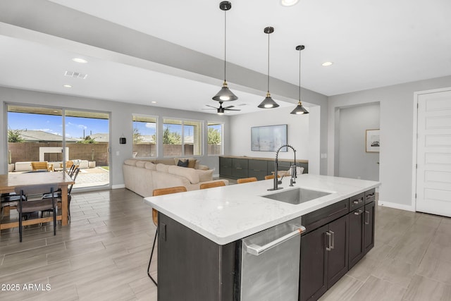 kitchen featuring stainless steel dishwasher, hanging light fixtures, a sink, an island with sink, and visible vents