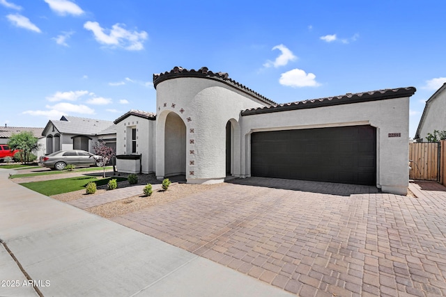 mediterranean / spanish house featuring stucco siding, an attached garage, decorative driveway, and a tile roof