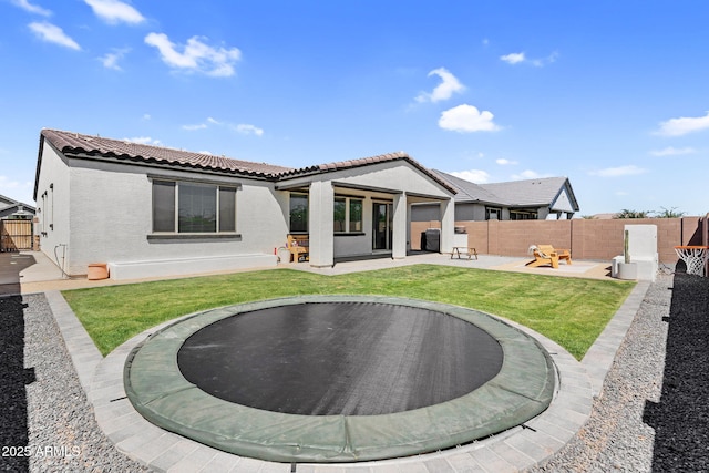 rear view of house featuring a fenced backyard, stucco siding, a tile roof, a patio, and a trampoline