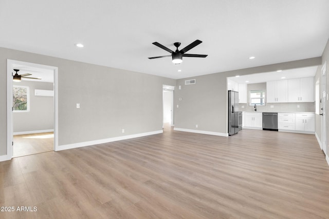 unfurnished living room with ceiling fan, sink, and light wood-type flooring