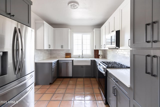 kitchen featuring appliances with stainless steel finishes, gray cabinetry, white cabinets, backsplash, and sink