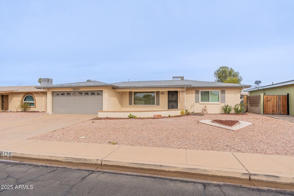 ranch-style home featuring stucco siding, an attached garage, driveway, and fence